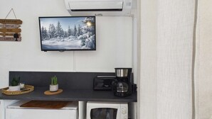 Et tekøkken med et fladskærms-tv, kaffemaskine, mikrobølgeovn og en lille potteplante.