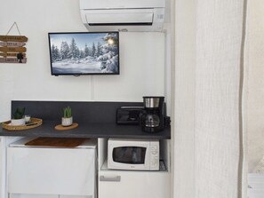 Eine Küchenzeile mit Flachbildfernseher, Kaffeemaschine, Mikrowelle und einem kleinen Topfpflanzen.
