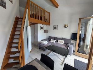 Ein kompakter Wohnraum mit Sofa, Couchtisch, Fernseher, Treppe und Kleiderschrank.