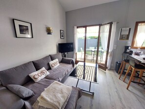 Ein Wohnzimmer mit einer Couch, einem Fernseher, einem Essbereich mit Stühlen und einer Glastür, die zu einem Außenbereich führt.