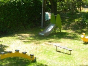 Une aire de jeux avec un toboggan, une balançoire jaune et une bascule verte.