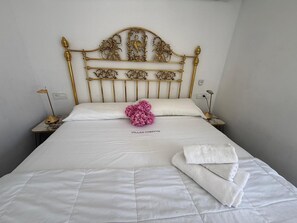 Un lit avec une tête de lit dorée, une literie blanche, une fleur rose et une serviette blanche pliée.