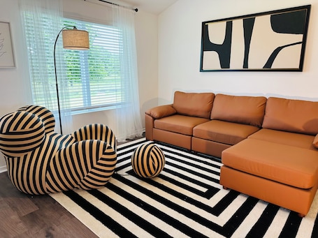 A living room with a striped sofa, a striped armchair, a round ottoman, a black and white striped rug, a floor lamp, and a large abstract painting on the wall.. Green Pastures - Another Blessing House