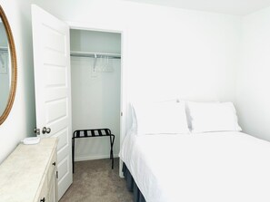 Een slaapkamer met een bed, nachtkastje, spiegel, kledingkast en een hangrek.