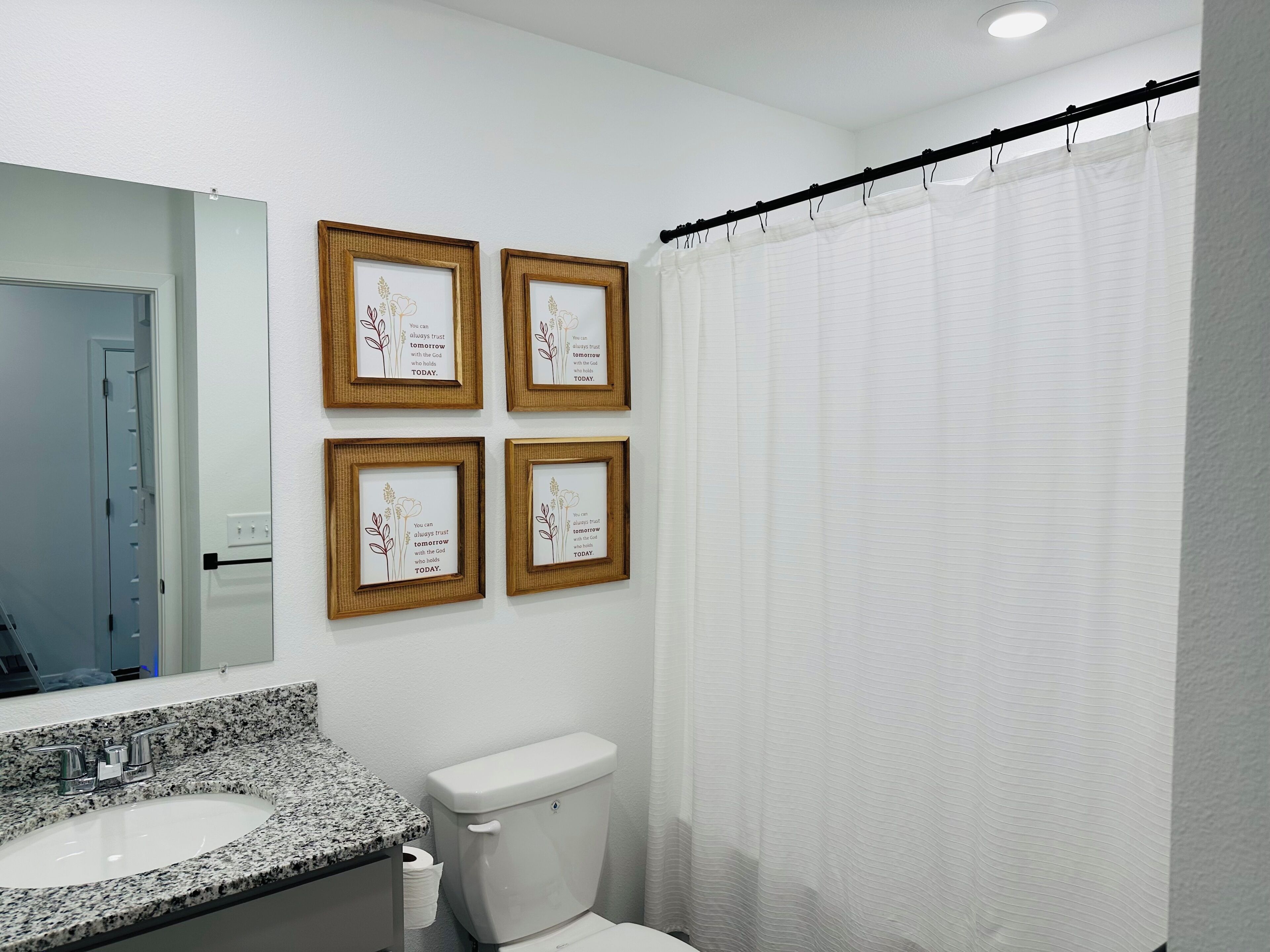 A bathroom with a white sink, toilet, and shower curtain. There are four framed inspirational quotes on the wall.