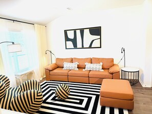 Una sala de estar con sofá, reposapiés, sillones a rayas, alfombra blanco y negro y un cuadro en la pared.