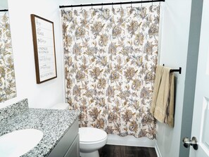 A bathroom with a floral shower curtain, a framed inspirational quote, and a granite countertop sink. - Green Pastures - Another Blessing House (Siloam Springs)