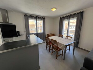 A compact kitchen with a dining area, including a table and chairs, a coffee maker, and a TV. - Apartment in city center, small sea view - 4 guests (Valras-Plage)