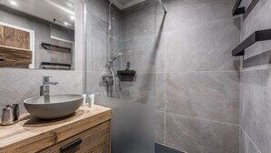 Un baño moderno con un lavamanos grande tipo lavabo, tocador de madera y zona de ducha con mampara de vidrio.