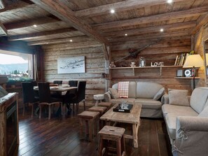 A rustic wooden interior with a dining area, sofa, and a wall-mounted shelf with decorative items. - Ski-in/Ski-out apartment - 4 guests (Courchevel 1850)
