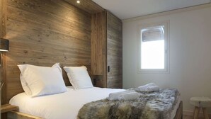 Una cama con ropa de cama blanca, un plaid de piel sintética y una ventana con persianas.