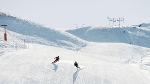 A snowy ski slope with skiers, ski lifts, and a clear sky. - Ski-in/Ski-out apartment - 4 guests (Courchevel 1850)