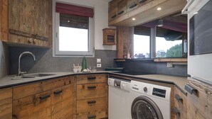 Una cocina con armarios de madera, lavadora integrada y ventana con persiana roja.