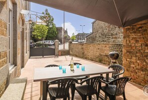 Eine Terrasse im Freien mit Tisch, Stühlen, einem Grill und einer Steinmauer.