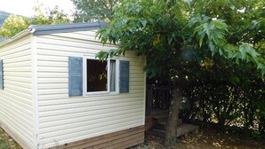 A small, single-story mobile home with a wooden deck and a tree in front. - Mobile home, pets allowed - 5 guests (Vesseaux)