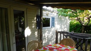 A covered patio with a table and chairs, a sliding glass door, and a window with shutters. - Mobile home, pets allowed - 5 guests (Vesseaux)