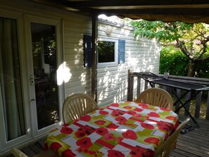 Eine überdachte Terrasse mit Tisch und Stühlen, eine Glastür zum Verschieben und ein Fenster mit Rollläden.
