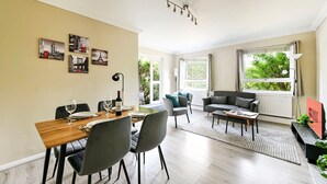 A modern living room with a dining area, large windows, and a view of greenery. - GuestReady - Comfortable 2bed in Richmond (London)