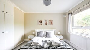 A bedroom with a bed, bedside tables, a window, and wall art. - GuestReady - Comfortable 2bed in Richmond (London)