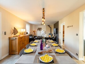 A dining area with a long table set for six, a wooden cabinet, a sofa, and a television on the wall.