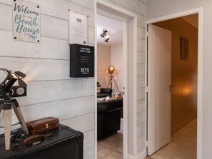 A room with a wooden wall, a welcome sign, a black storage box, a desk lamp, and a door leading to another room.