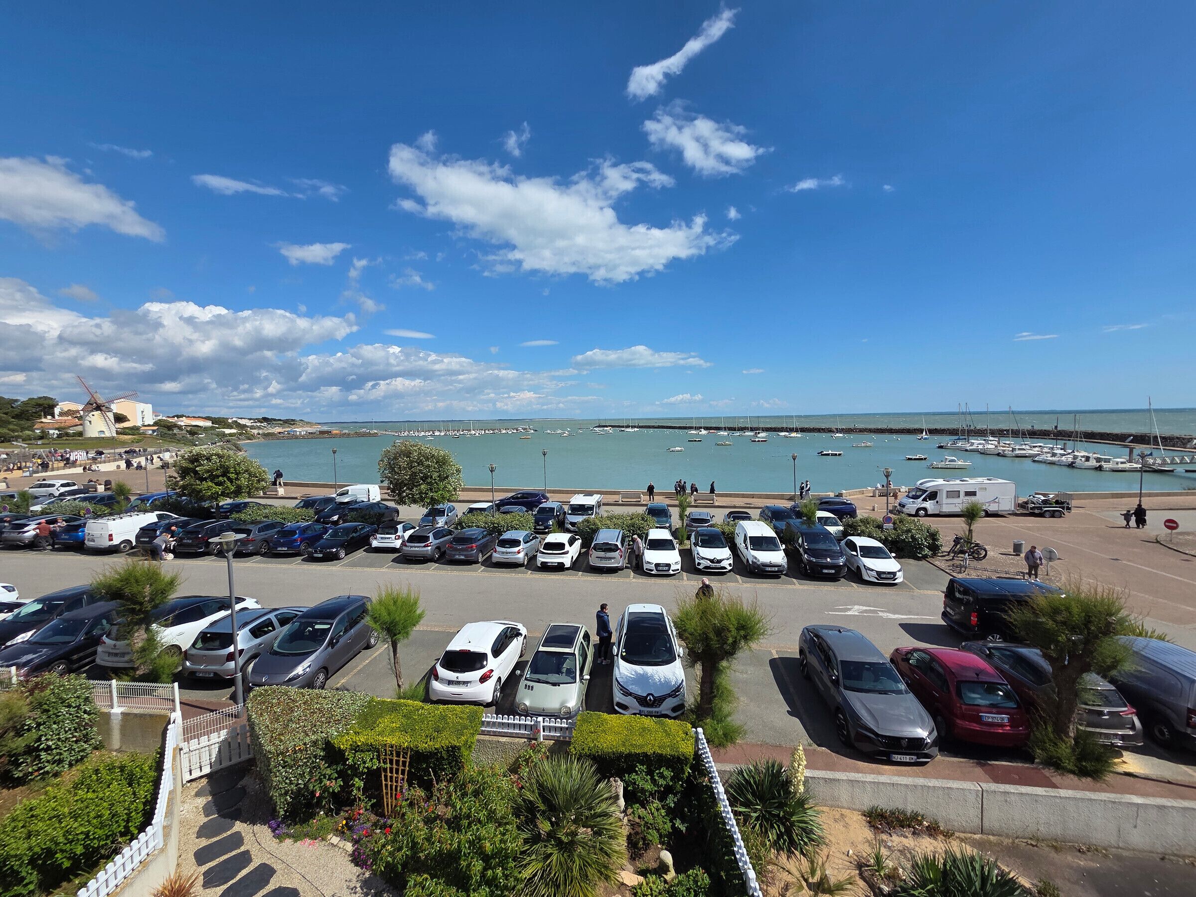A parking lot with various cars and a marina in the background.