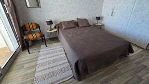 Un dormitorio con una cama, una silla, dos mesitas de noche con lámparas, un espejo y una alfombra estampada.
