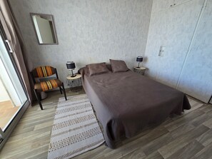 A bedroom with a bed, a chair, two bedside tables with lamps, a mirror, and a patterned rug. - Apartment with port view - 4 guests (Jard-sur-Mer)