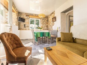 A cozy living room with a stone wall, a green sofa, a patterned armchair, and a wooden coffee table. - Peaceful cottage in the countryside, pets welcome (GUENROUET)