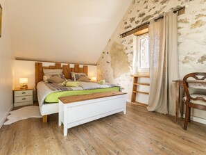 A bedroom with a wooden headboard, a bed with striped bedding, a bedside table with a lamp, a wooden bench, and a chair. - Peaceful cottage in the countryside, pets welcome (GUENROUET)