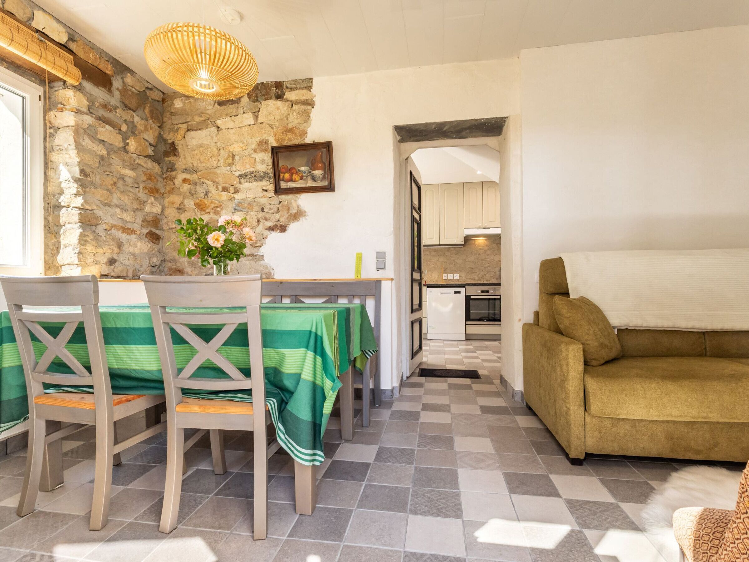 A dining area with a stone wall, a table with chairs, a sofa, and a kitchen in the background.