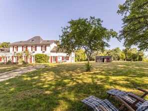 A large white building with red shutters, a tree in the foreground, and a small structure in the background. - Peaceful cottage in the countryside, pets welcome (GUENROUET)