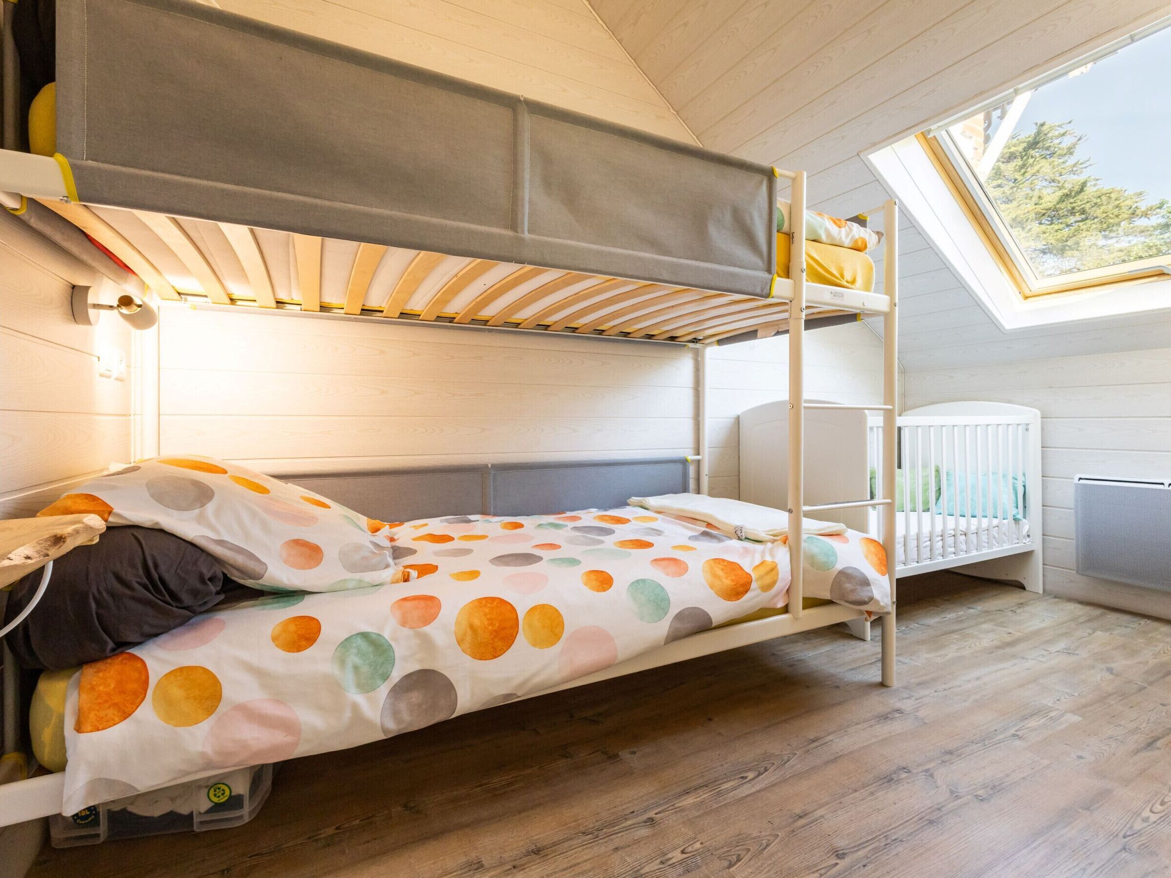 Un lit superposé avec une couvre-lit à pois, un berceau et une lucarne.