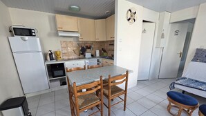 Une cuisine compacte équipée d’un four à micro-ondes, d’un réfrigérateur et d’une cuisinière. On y trouve une table à manger avec des chaises, ainsi qu’un petit coin salon avec des coussins.