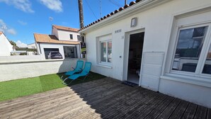 Une terrasse en bois avec deux chaises bleues, un bâtiment blanc avec un toit en tuiles et un ciel dégagé.