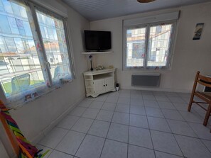Habitació amb sòcols de rajola, un armari blanc, un televisor fixat a la paret i una finestra amb vista a edificis.