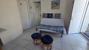 Une chambre à coucher comprenant un lit, deux tabourets, un luminaire suspendu, une porte et un tableau accroché au mur.