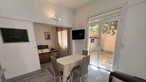 Una habitación con una mesa de comedor, sillas, un sofá, un televisor y un ventanal corredera que da a un espacio exterior.