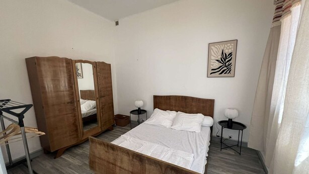Un dormitorio con una cama de madera, un armario, una mesita de noche, una lámpara y una obra de arte en la pared.