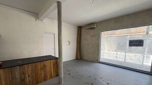 Una habitación con mostrador de madera, puerta blanca, pilar de concreto y un amplio ventanal con vista a la calle.