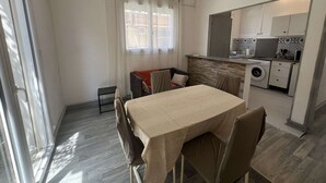 Cocina compacta con lavadora, comedor con mesa y sillas, y puerta corrediza de vidrio que da a un balcón.