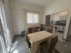 A compact kitchen with a washing machine, a dining area with a table and chairs, and a sliding glass door leading to a balcony. - Charming T2 city center, garden - 2 guests (Valras-Plage)
