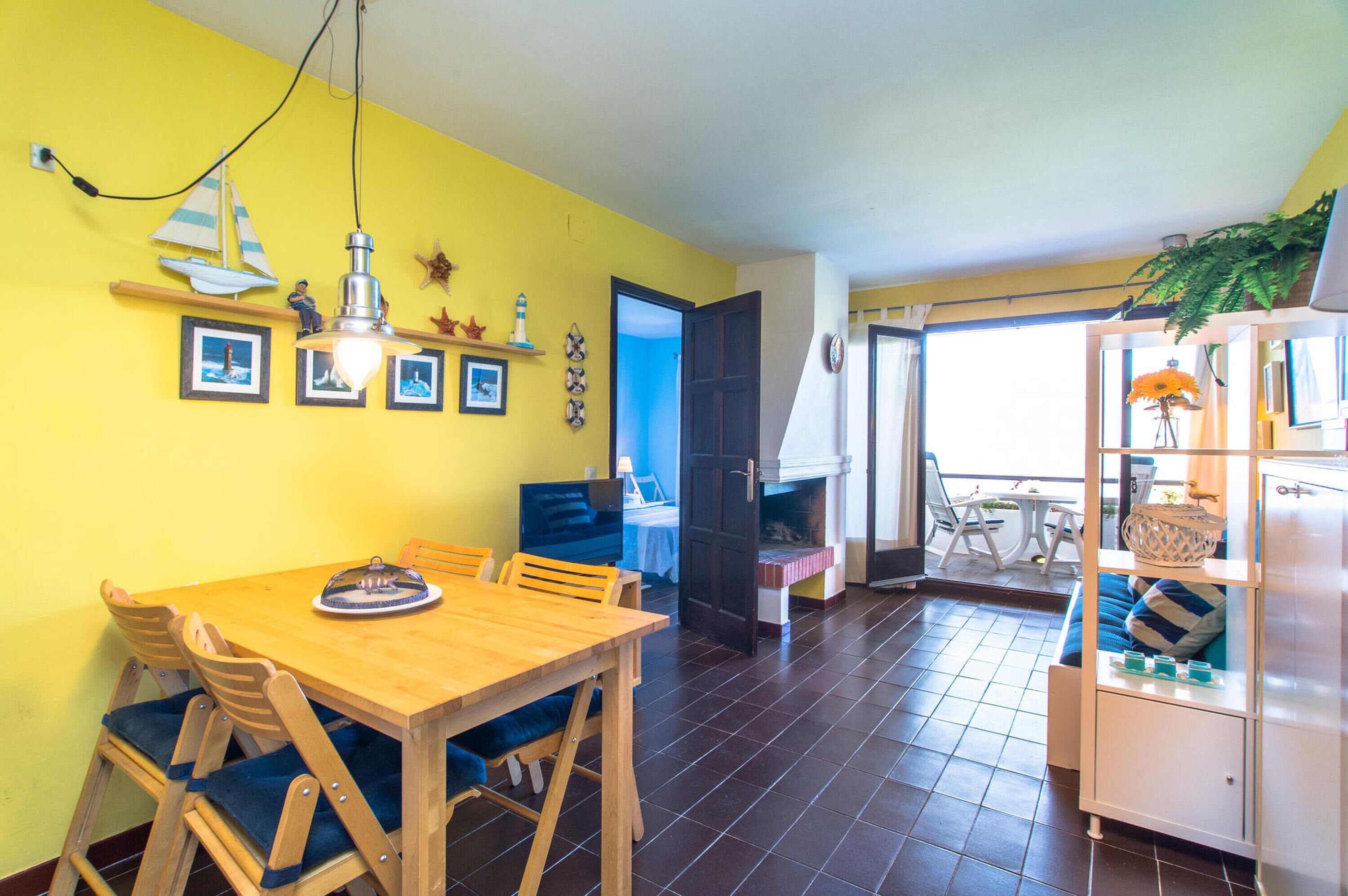 A dining area with a wooden table and chairs, a kitchen with a stove, and a balcony with outdoor seating.
