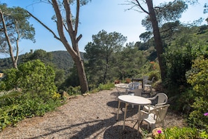 A gravel patio with outdoor seating, surrounded by trees and vegetation. - Apartment in Sa Tuna with views (Begur)