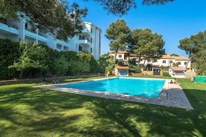 A swimming pool with a stone border, surrounded by a grassy lawn and trees. - Apartment in Sa Tuna with views (Begur)