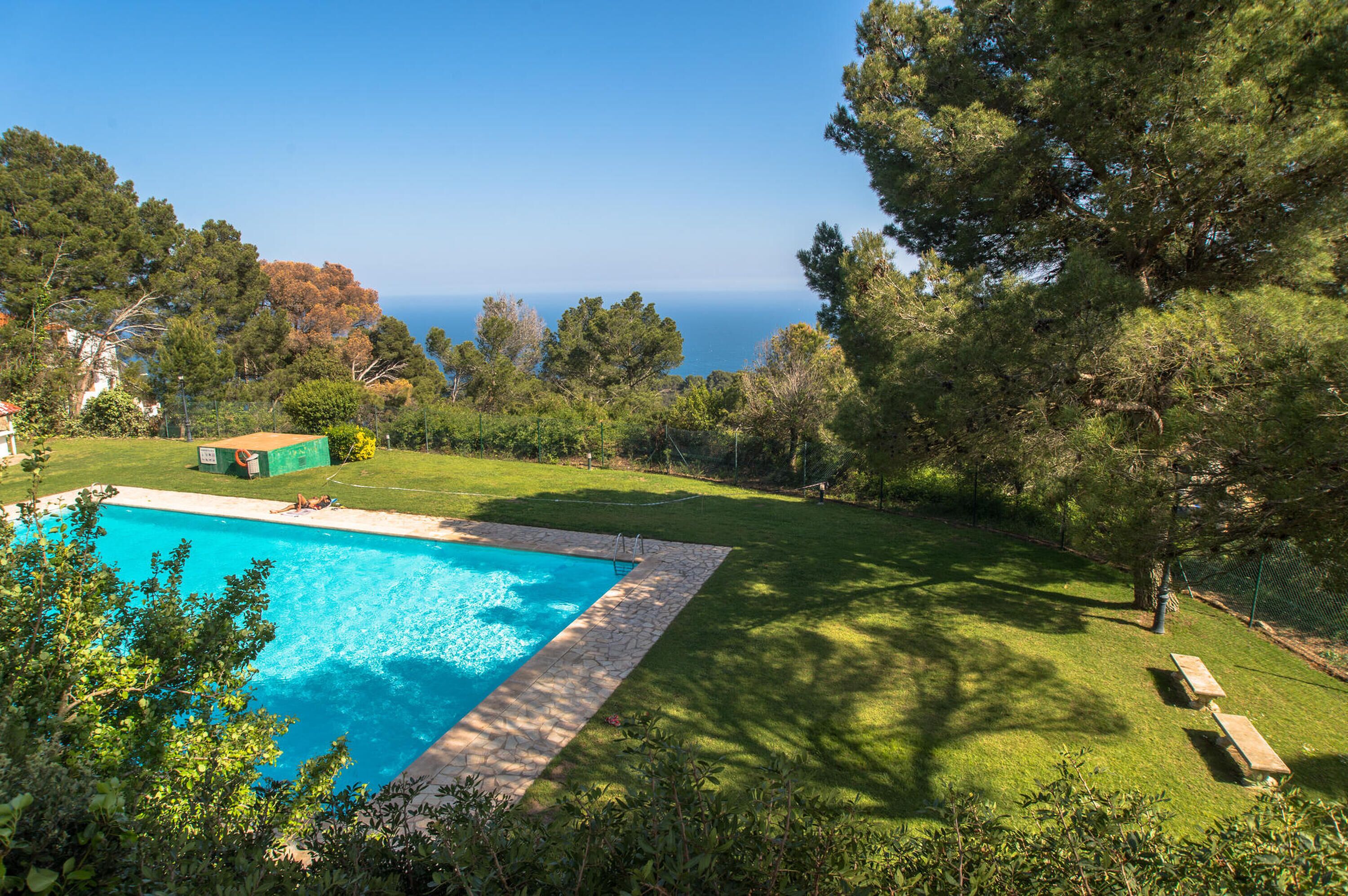 A swimming pool surrounded by a well-maintained lawn, trees, and a view of the sea.