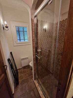 Een badkamer met een douche, toilet, raam en radiator.