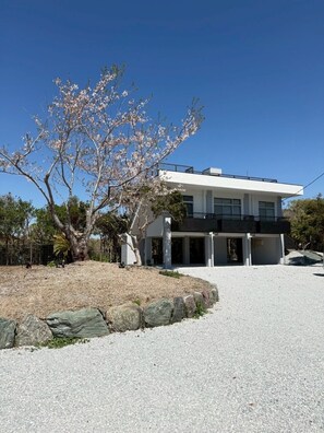 Una casa moderna de dos pisos con fachada blanca, un balcón y un camino de entrada de grava.