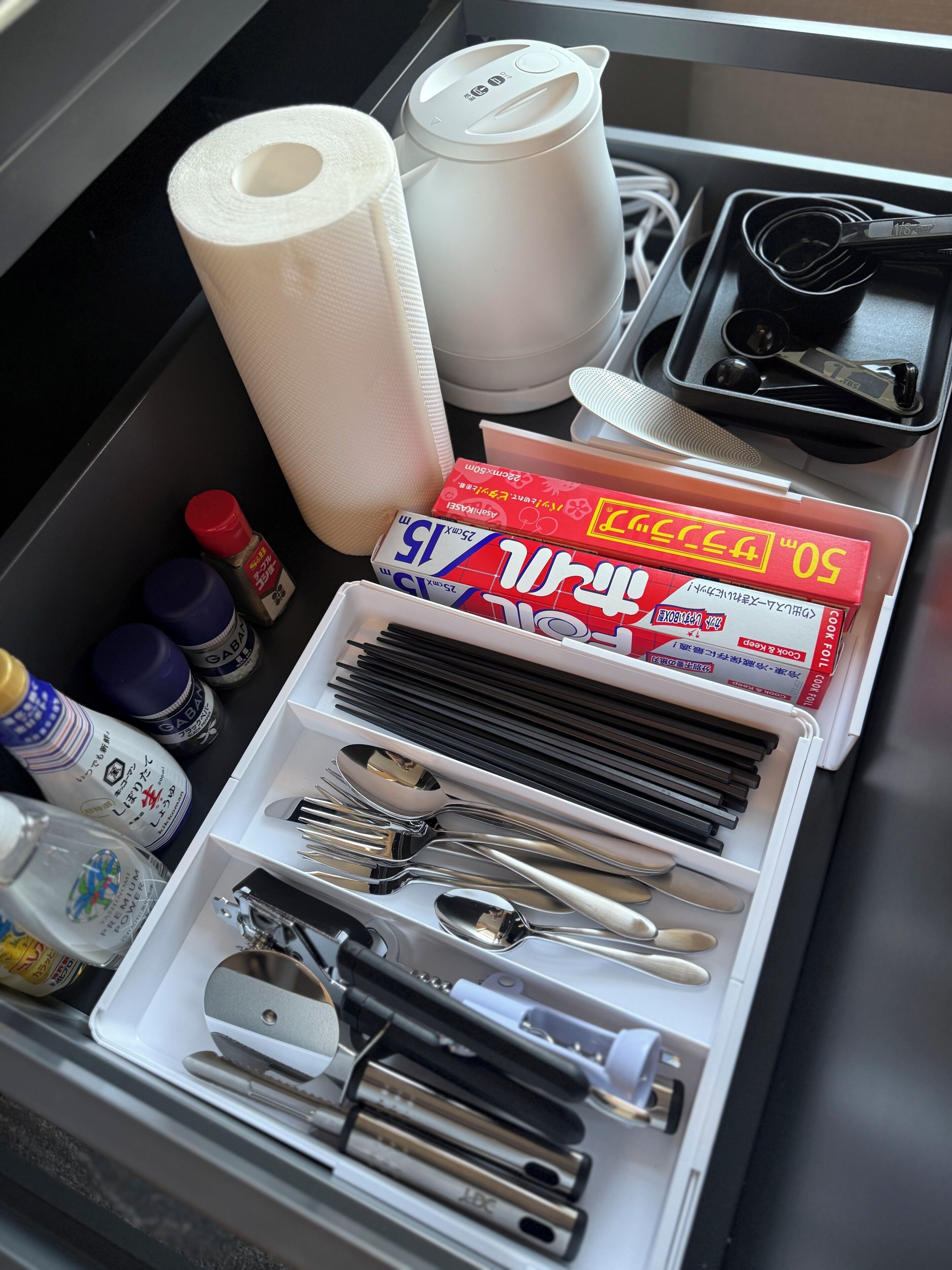 Un cajón con utensilios de cocina ordenados, incluyendo palillos, cucharas y una tetera.