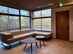 Un interior moderno con un sofá modular, una pequeña mesa redonda, ventanas amplias y una puerta de madera.